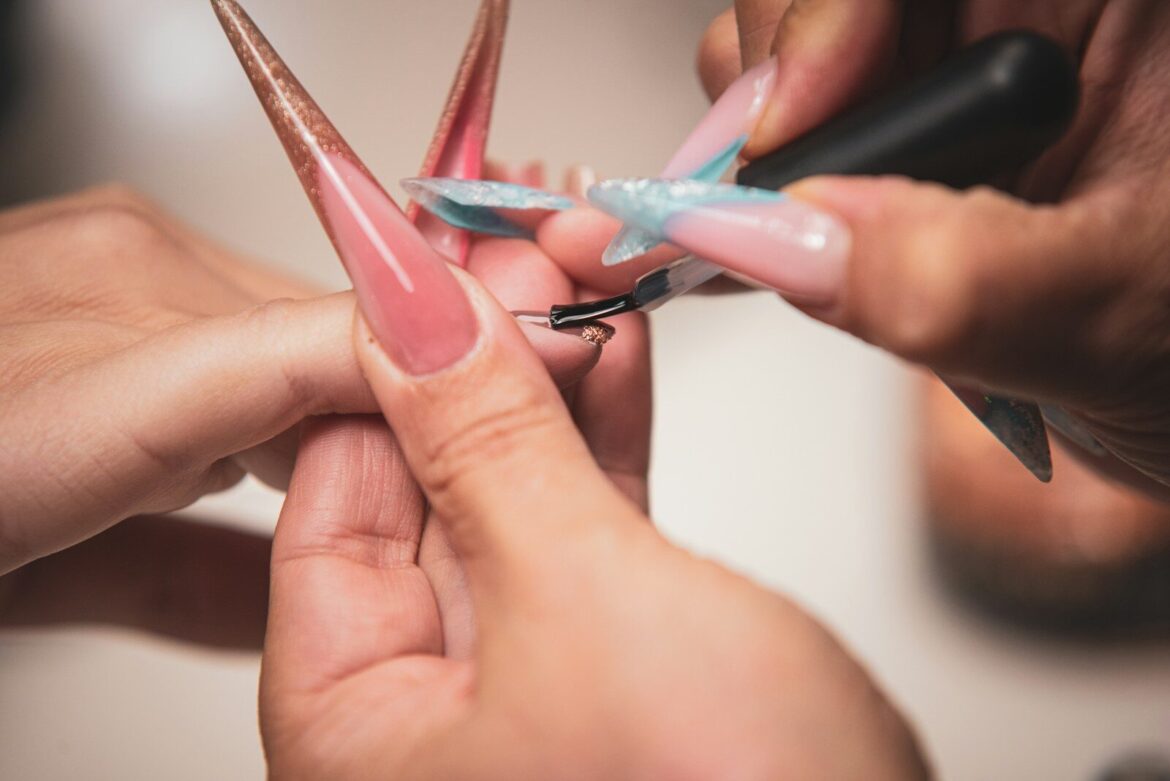 Nagelterapeut som lackar långa naglar på en kunds hand